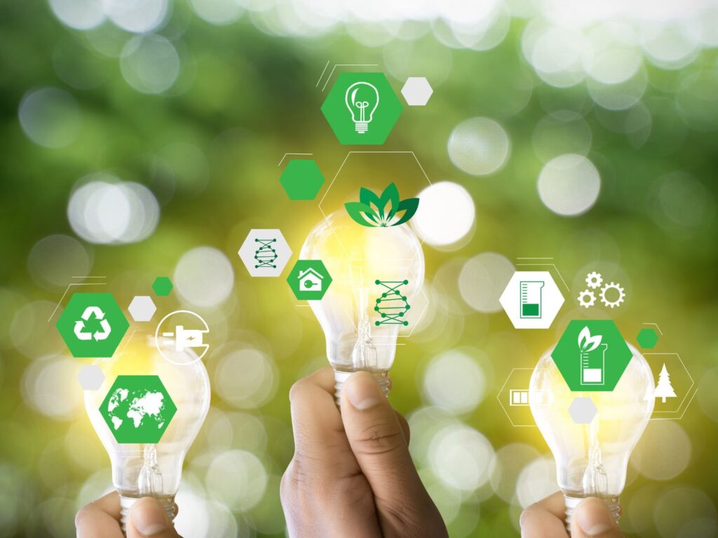 Três mãos segurando lâmpadas com ícones de energia limpa, reciclagem e meio ambiente, simbolizando inovação e a importância da embalagem consciente.