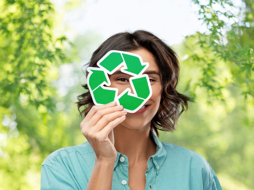 A foto de uma mulher segurando um símbolo de reciclagem reforça a ideia de que o que é marketing empresarial com foco em sustentabilidade tem o consumidor como parte ativa desse processo. A comunicação aqui é direta e visual, incentivando a participação e a conscientização.