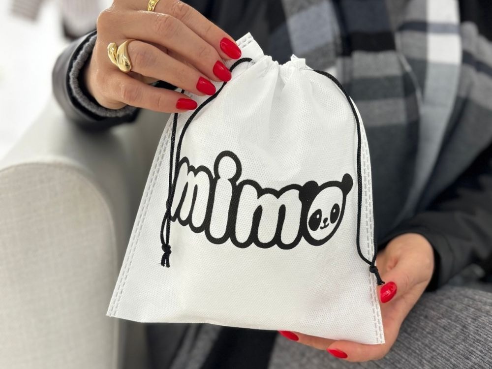 Pessoa segurando uma sacola de tecido branco personalizada com a palavra “mimo” e ilustração de um panda.