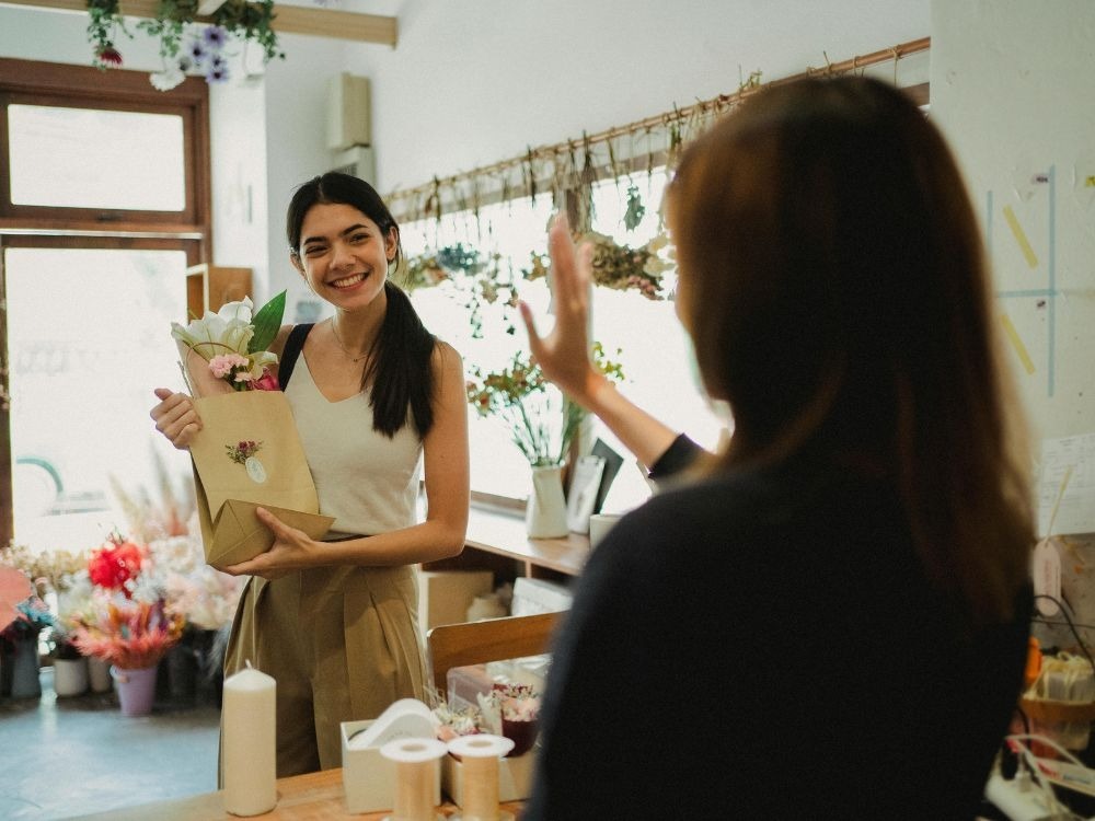 Cliente recebendo flores em embalagem decorada. Gestos simples como flores personalizadas fazem parte das 6 ideias para presentear clientes e fidelizar.