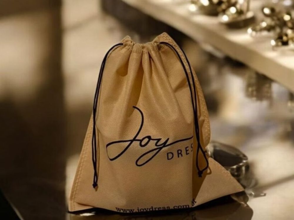 Sacola de tecido bege com logotipo Joy Dress. Brindes sustentáveis e personalizados estão entre as 6 ideias para presentear clientes e fortalecer a marca.