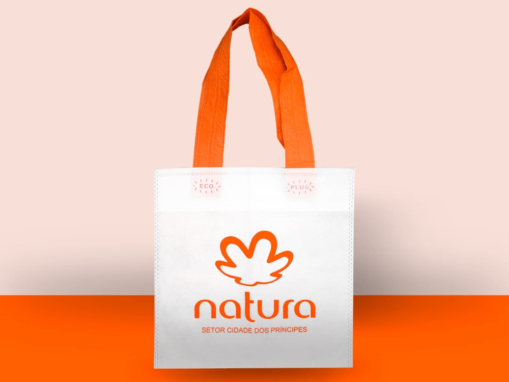 Ecobag de TNT branca com alças laranja e logotipo personalizado, ideal para ações promocionais e embalagens reutilizáveis.