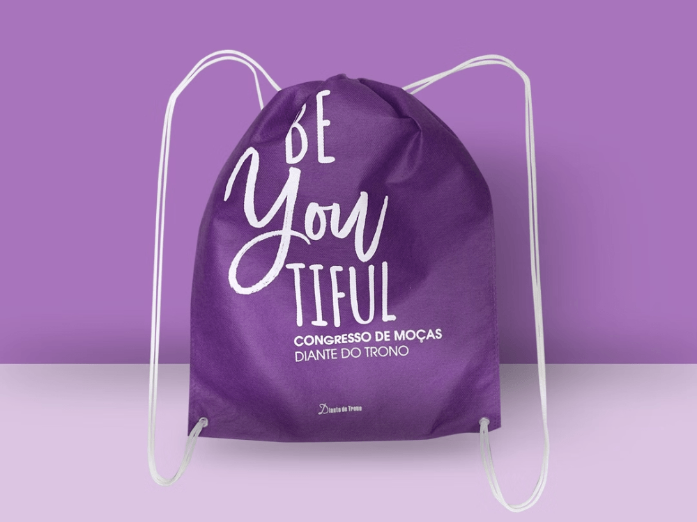 Mochila saco confeccionada em TNT roxo com impressão personalizada e cordões brancos, indicada para eventos e brindes ecológicos.