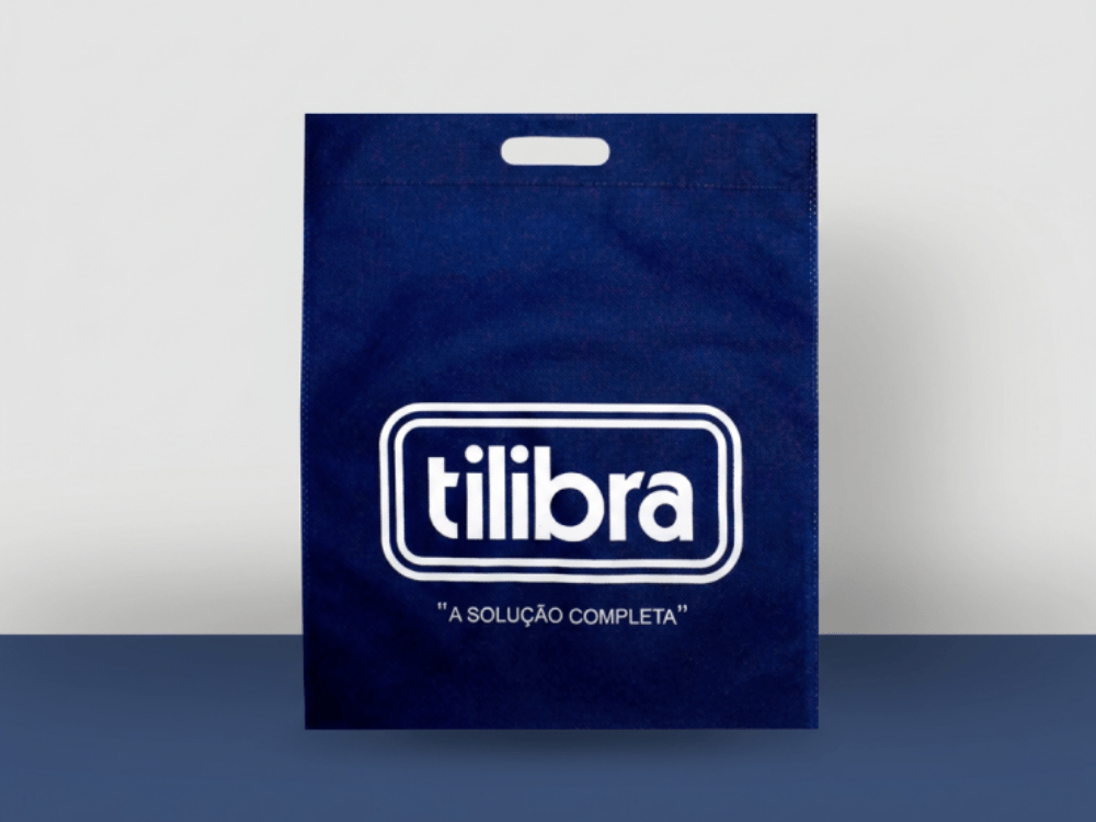 Sacola de tecido TNT azul com alça vazada e logotipo branco, apresentada sobre uma superfície clara. Tudo para explicar como passar tecido TNT.