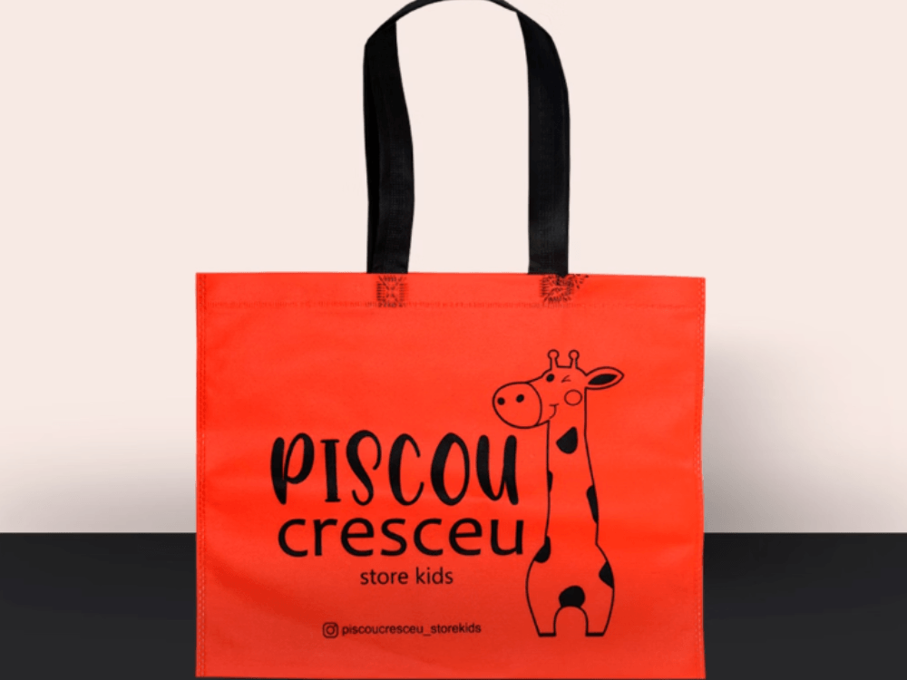 Sacola reutilizável vermelha da Piscou Cresceu Store Kids, com alças pretas e ilustração de uma girafa impressa na frente.